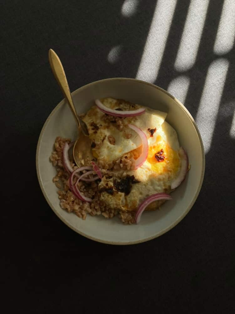 Bowl of food with a spoon on a dark surface with Bé Na Chili Oil