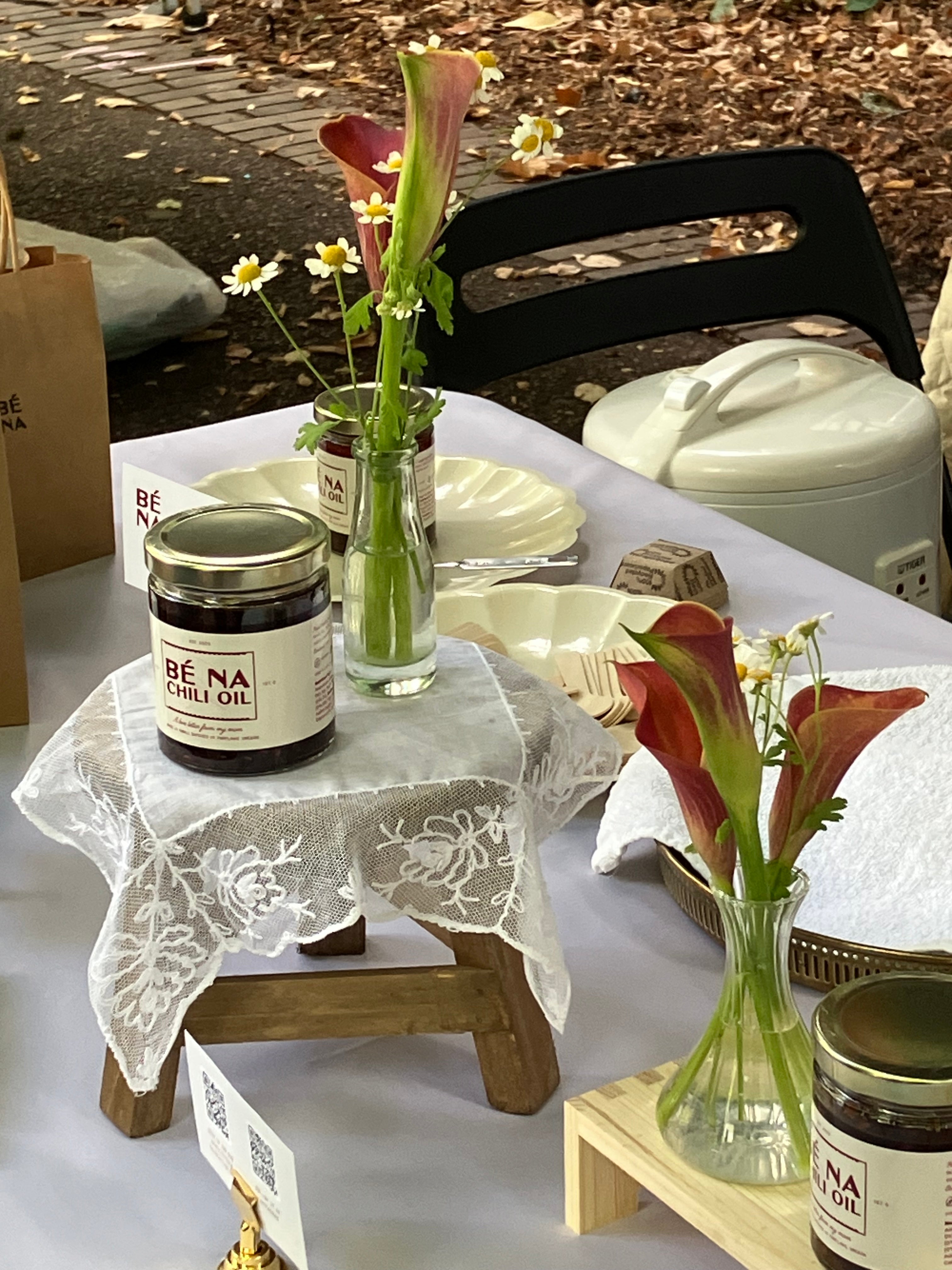 Table setting with jars of Bé na oil and decorative vases on a lace tablecloth.