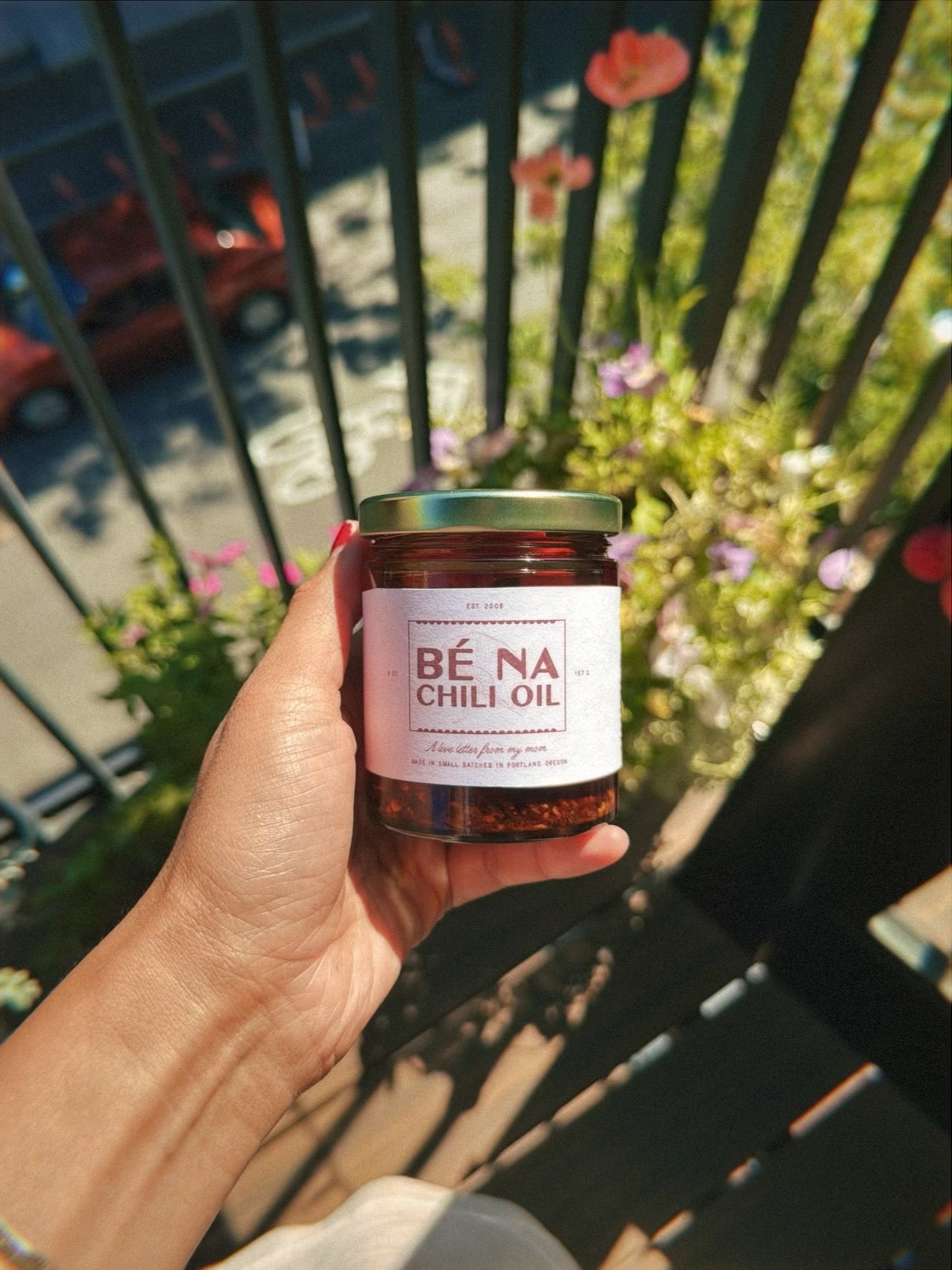 Hand holding a jar of Bé Na Chili Oil with a blurred outdoor background